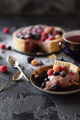 Homemade ricotta pie with frozen berries and sugar icing served with silver spoons and karkade tea on black background. Low key still life