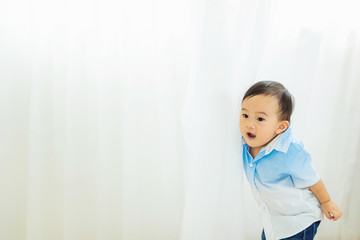 Cute little happy baby playing hide and seek in white curtain with free text copy space.