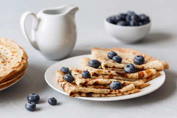 Thin pancakes on white plate with blueberries and sour cream. Grey background. Close up.