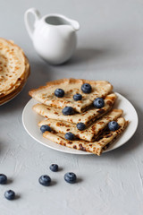 Thin pancakes on white plate with blueberries and sour cream. Grey background. Close up.