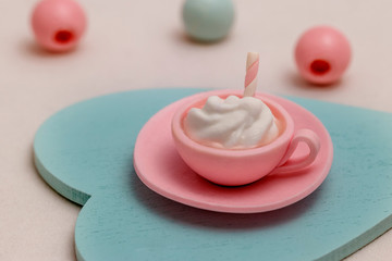 Products from polymer clay: a cup with a dessert with marshmallows, meringues and macaroons in pastel blue and pink colors on a decorative wooden heart.