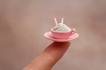 Miniature: delicious dessert - a small plate with a mug with marshmallows and waffles made of polymer clay at the tip of the finger of a female hand.