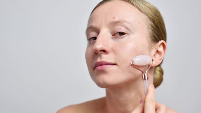 Woman without makeup is getting massage face using jade roller.