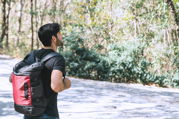 Close up rear view of young caucasian man in black t-shirt with backpack standing and looking to...