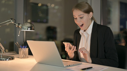 The Successful Businesswoman Scrolling on Smartphone in Office at Night