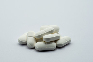 A Number of white medical tablets lying on a white surface and on a white background.
