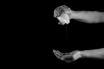 Disinfecting hands with alcohol, hands with bottle of medical alcohol isolated on black, copy space