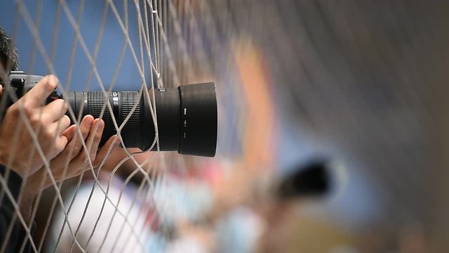 Photographer lens is seen through a safety net during a photo coverage of a sport match