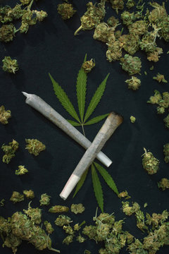 Cannabis background: Top view of marijuana joints and leaves surrounded by weed buds on black background.