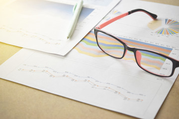 Naklejka na ściany i meble Financial graphs and charts with eyeglasses and pen on desk.