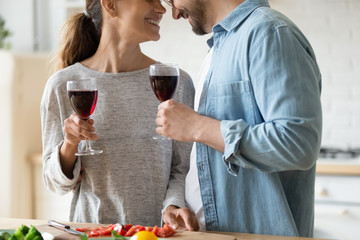 Close up happy loving couple holding glasses, drinking red wine, smiling young woman and man touching foreheads, enjoying romantic date, standing in kitchen, celebrating relocation or anniversary