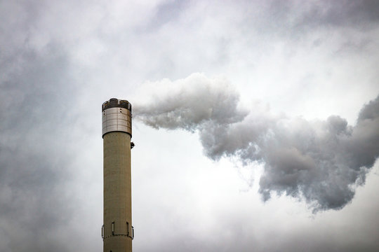 Tall chimney emitting gases into the atmosphere, causing air pollution. Gray, dramatic cloudy sky.