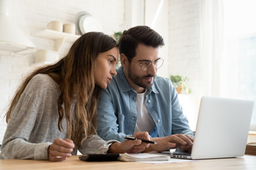 Focused young couple calculating bills, discussing planning budget together, serious wife and...