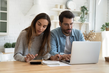 Serious man and woman calculating bills, using calculator and laptop, online banking services,...