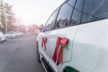 Wedding decorated car. Two red bows on the door handles of a car. In the background is a wedding motorcade