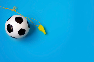 Fototapeta na wymiar Miniature soccer ball and yellow whistle on a blue background. World championship. Referee and football player. Physical development of the child. How much does health cost? Sports and money.