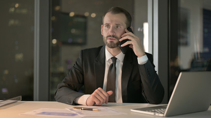 The Ambitious Businessman talking on Smartphone in Office at Night