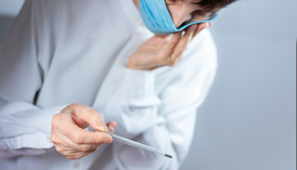 Coronavirus quarantine and Air pollution pm2.5 concept. Old sick woman wearing respirator mask for protect holds thermometer. Wuhan, China epidemic virus symptoms background.