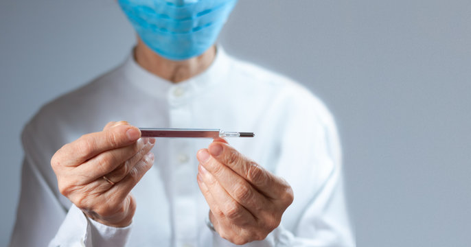 Coronavirus quarantine and Air pollution pm2.5 concept. Old sick woman wearing respirator mask for protect holds thermometer. Wuhan, China epidemic virus symptoms background.