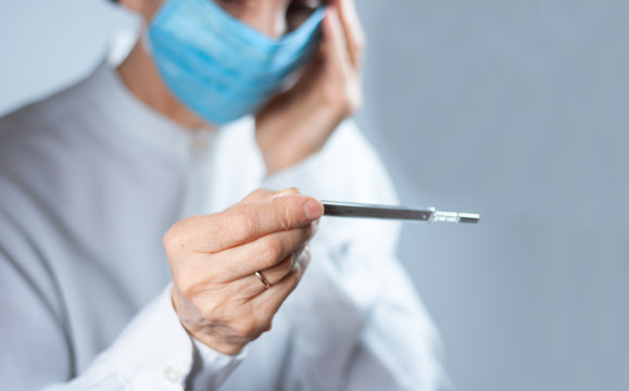 Coronavirus quarantine and Air pollution pm2.5 concept. Old sick woman wearing respirator mask for protect holds thermometer. Wuhan, China epidemic virus symptoms background.