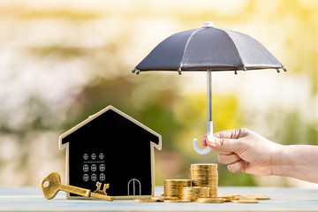 Blackboard house and stacked gold coin and master key and woman hand hold the black umbrella for protect on sunlight in the public park, Saving money for real estate and property protection concept.