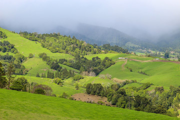 Obraz premium Lush green mountain landscape with fog and clouds hugging mountains