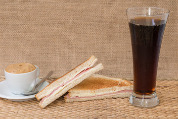 Un sándwich de jamón y queso york con un vaso de cola y un café.