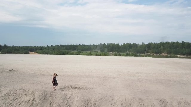 Girl in a sundress walks along the edge of a sand pit