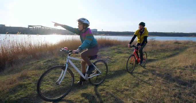 Couple of male and female ride on bicycles near river during sunset