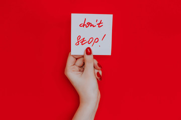 Note in a female hand with manicure, red nails. "Don't stop!" sign. Background red