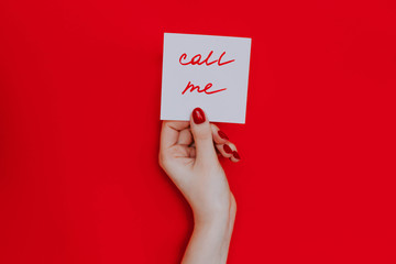 Note in a female hand with manicure, red nails. "Call me" sign. Background red
