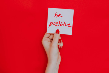 Note in a female hand with manicure, red nails. "Be positive" sign. Background red