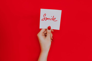 Note in a female hand with manicure, red nails. "Smile" sign. Background red