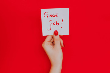 Note in a female hand with manicure, red nails. "Good job!" sign. Background red