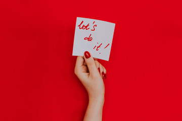 Note in a female hand with manicure, red nails. "Let's do it!" sign. Background red