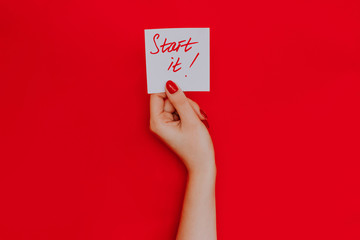 Note in a female hand with manicure, red nails. "Start it!" sign. Background red