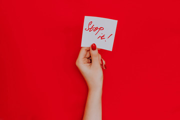 Note in a female hand with manicure, red nails. "Stop it!" sign. Background red