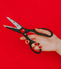 Female hand with red manicure holding a kitchen scissors on a red background. Concept: Feminism, Trimming Rights