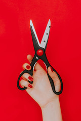 Female hand with red manicure holding a kitchen scissors on a red background. Concept: Feminism, Trimming Rights
