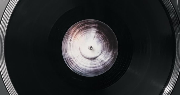 Black vinyl record on DJ player. Black vinyl background black, white label in center. Rotating plate close-up on turntable. Macro Top view. Popular styles of disco from the 60s, 70s, 80s, 90s. Party
