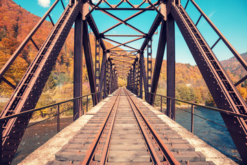 Old railway on the bridge over the mountain river in autumn