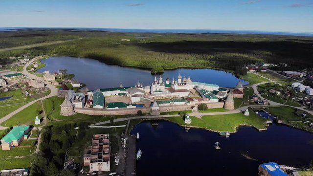 Smooth cinematic fly-by of the Solovetsky monastery from the seaside with a view over village and island on the sunny day. Solovetsky monastery is an old (1420) ROC monastery.
