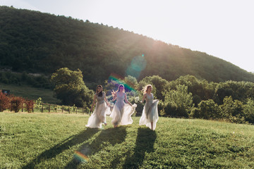 Bridesmaids in white dresses run on the green grass against the backdrop of the mountains.
