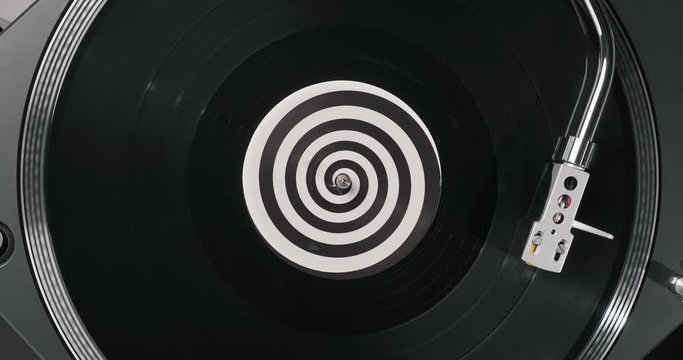 Black vinyl record on DJ player. Black vinyl background spiral label in center. Rotating plate close-u on turntable. Needle stylus. Macro Top view. Popular styles of disco 60s, 70s, 80s, 90s. Party