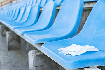 A medical mask is lying on a stadium chair. Empty stands.Protection of the crown from viruses and bacteria ceases. Cancellation of sporting events. Rows of chairs in an open stadium. copy space.