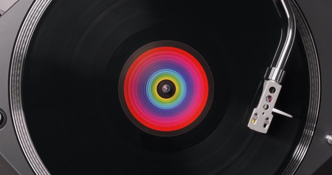 Black vinyl record DJ player. Black vinyl background with color spectrum label in center. Rotating plate close-up on turntable. Needle stylus. Top view. Popular styles of disco from 60s, 70s, 80s, 90s