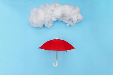 Red toy umbrella under a puffy cotton cloud on a sky blue background