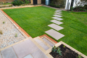New turf installation around a new stepping stone pathway to a pebbled area and patio with steps. All part of a garden landscaping desing project. - 330567200
