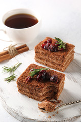 Dessert. Chocolate biscuit cake with cream, cinnamon and berries. Sweet pie with cocoa and chocolate on a white wooden board. Cup of coffee and rosemary on a light background. Copy space