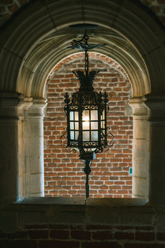 An antique lamp, framed by a stone arch window with a brick wall background